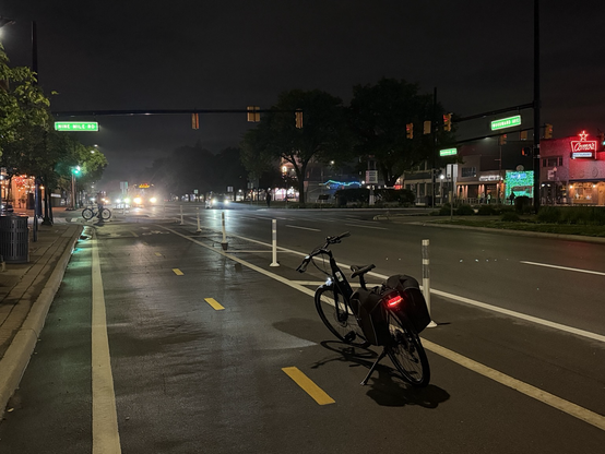 My bike on the Woodward cycle track in downtown Ferndale at night, looking north toward 9 Mile. Headlights from light traffic are reflecting on the wet pavement.